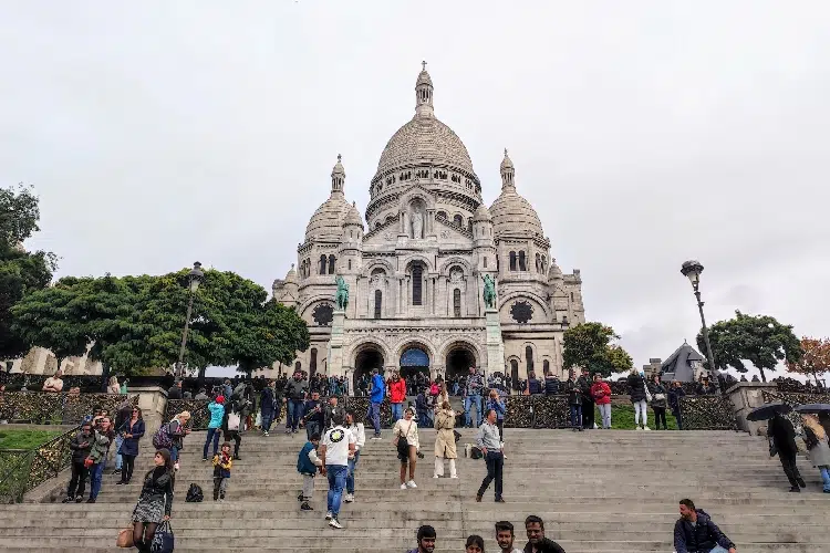 Basílica em cor clara, frente a uma escadaria com turistas.