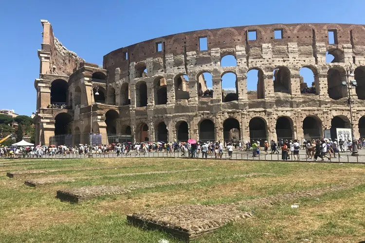 Dia de céu azul com fila de turistas em frente ao Coliseu de Roma.