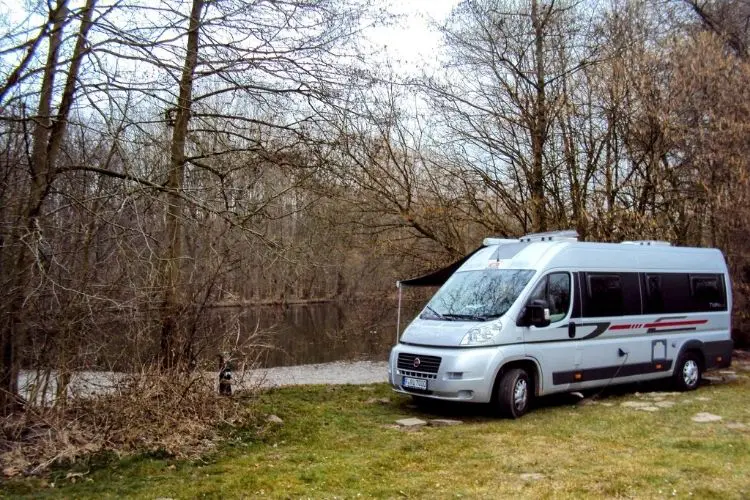 Motorhome estacionado na natureza com rio ao fundo e árvores sem folhas